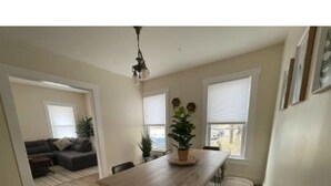 A dining area with a wooden table, chairs, a chandelier, and potted plants. - Green Mountain Retreat (Rutland)