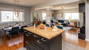 A modern kitchen with a central island, dining area with chairs, a sofa, and a TV. - ✪ Ramsay Manor - Walk to Stampede in 10 mins ✪ (Calgary)