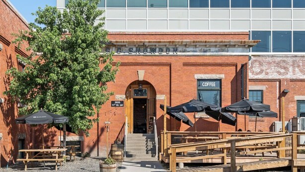 A brick building with a coffee shop sign, outdoor seating with umbrellas, and a staircase leading to the entrance. - ✪ Ramsay Manor - Walk to Stampede in 10 mins ✪ (Calgary)