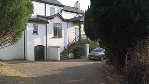 A two-story house with a paved driveway, a car parked in front, and a staircase leading to the entrance. - Room-tranquil Ensuite Room With Garden V (Londonderry)