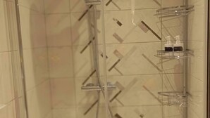 A glass-enclosed shower with a handheld showerhead, a glass shelf with toiletries, and a white sink with a drain cover. - Room-tranquil Ensuite Room With Garden V (Londonderry)