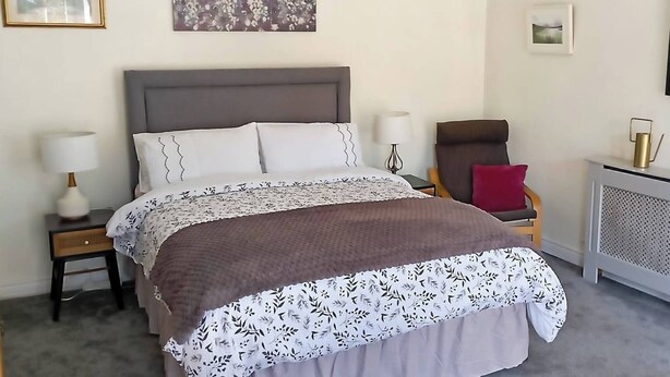 A neatly arranged bedroom with a bed, bedside tables, a chair, and artwork on the walls. - Room-tranquil Ensuite Room With Garden V (Londonderry)