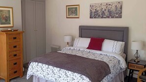 A bedroom with a bed, a dresser, a radiator, and two wall-mounted lamps. - Room-tranquil Ensuite Room With Garden V (Londonderry)