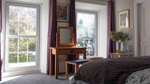 A bedroom with a bed, a wooden desk with a mirror, and a chair. There is a window with curtains, a door, and a plant on the wall. - Room-tranquil Ensuite Room With Garden V (Londonderry)
