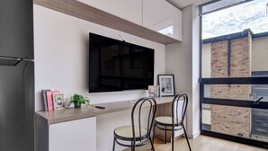 Una cocina moderna con televisor de pantalla plana, dos sillas, una mesita y un ventanal con vistas a un edificio de ladrillo.