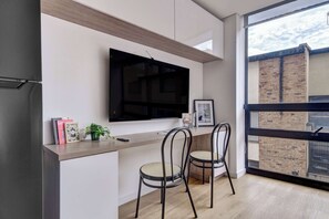 A modern kitchen with a flat-screen TV, two chairs, a small table, and a window with a view of a brick building. - w* | Loft Hideaway in the Heart of Bogotá (Bogotá)