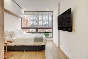 A modern bedroom with a large window, a bed, a round table, and a mounted TV. - w* | Urban Loft in the Heart of Bogotá (Bogotá)