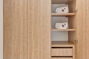Ein Holzschrank mit drei Einlegeböden, auf jedem ein weißes Handtuch mit einem schwarzen 'W'.