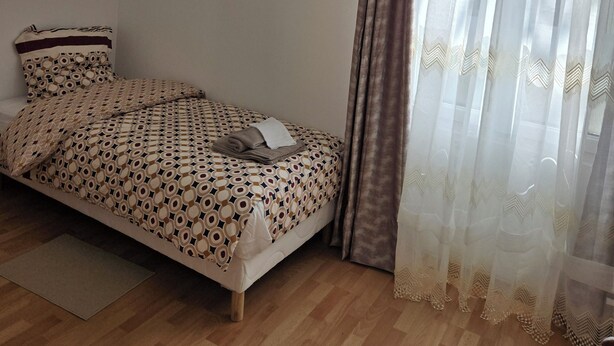 A single bed with a patterned bedspread, a hanging pink lamp, sheer curtains, and a wooden floor. - Sejour eau vive, 3 bedrooms Near metro and créteil village (Créteil)
