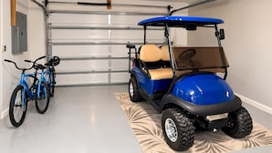 En garage med en blå golfbil, to cykler og en garageport.
