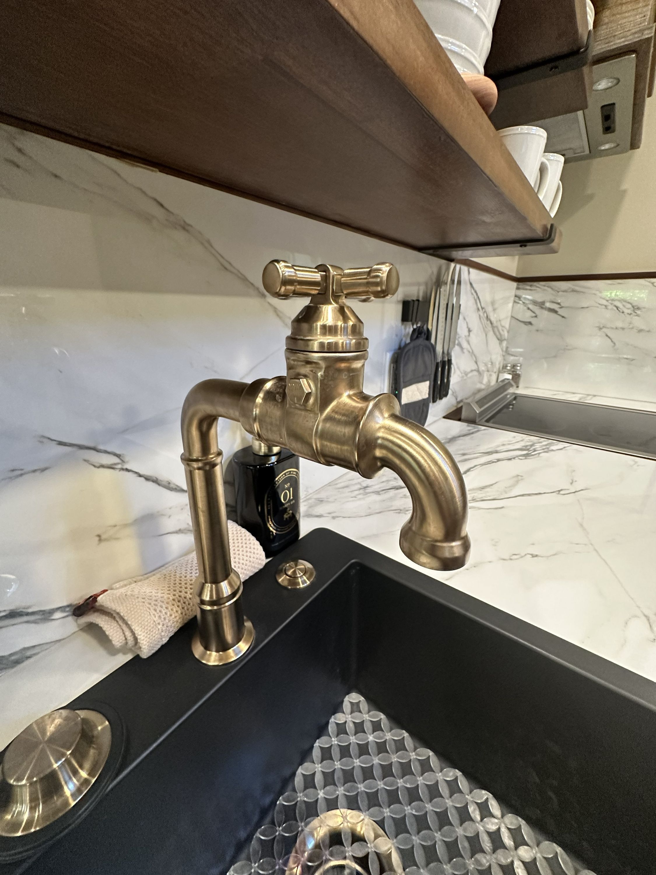 A kitchen sink with a brass faucet, a black countertop, and a marble backsplash.