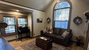 Ein geräumiges Wohnzimmer mit großem Fenster, einem dunkelbraunen Sofa, einem Holztisch und einem Essbereich im Hintergrund.
