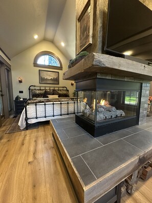 A bedroom with a fireplace, a bed with a headboard, a window, and a painting on the wall. - Luxury Gold Miner Cottage Walk to Britt (Jacksonville)
