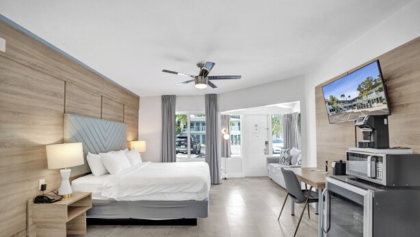 Habitación de hotel moderna con cama, escritorio, televisor y kitchenette.
