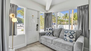 Una habitación con un sofá gris, una lámpara de pie y una puerta que da al exterior.