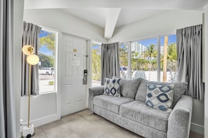 A room with a grey sofa, a floor lamp, and a door leading outside. - The Botanica (Fort Lauderdale)