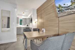 A modern hotel room with a wooden accent wall, a dining area with a table and chairs, a kitchen in the background, and a view of the hotel exterior. - The Botanica (Fort Lauderdale)