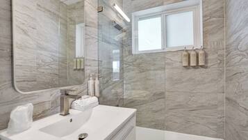 Un baño moderno con pared de mármol, un espejo grande, un lavamanos y una ventana.