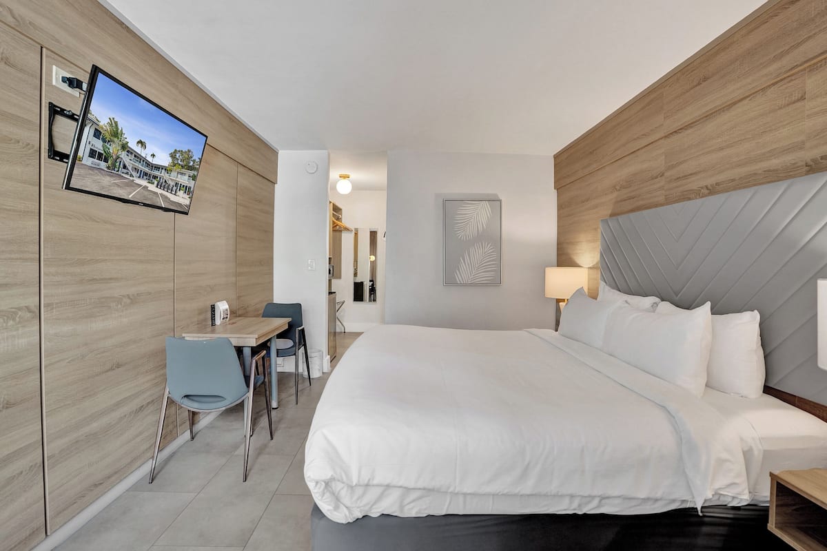 A hotel room with a bed, a desk, a chair, a TV mounted on the wall, and a view of the outside.
