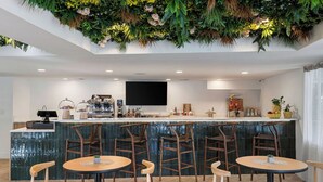Un área de bar moderna con una pared verde, sillas de madera y un televisor de pantalla plana.