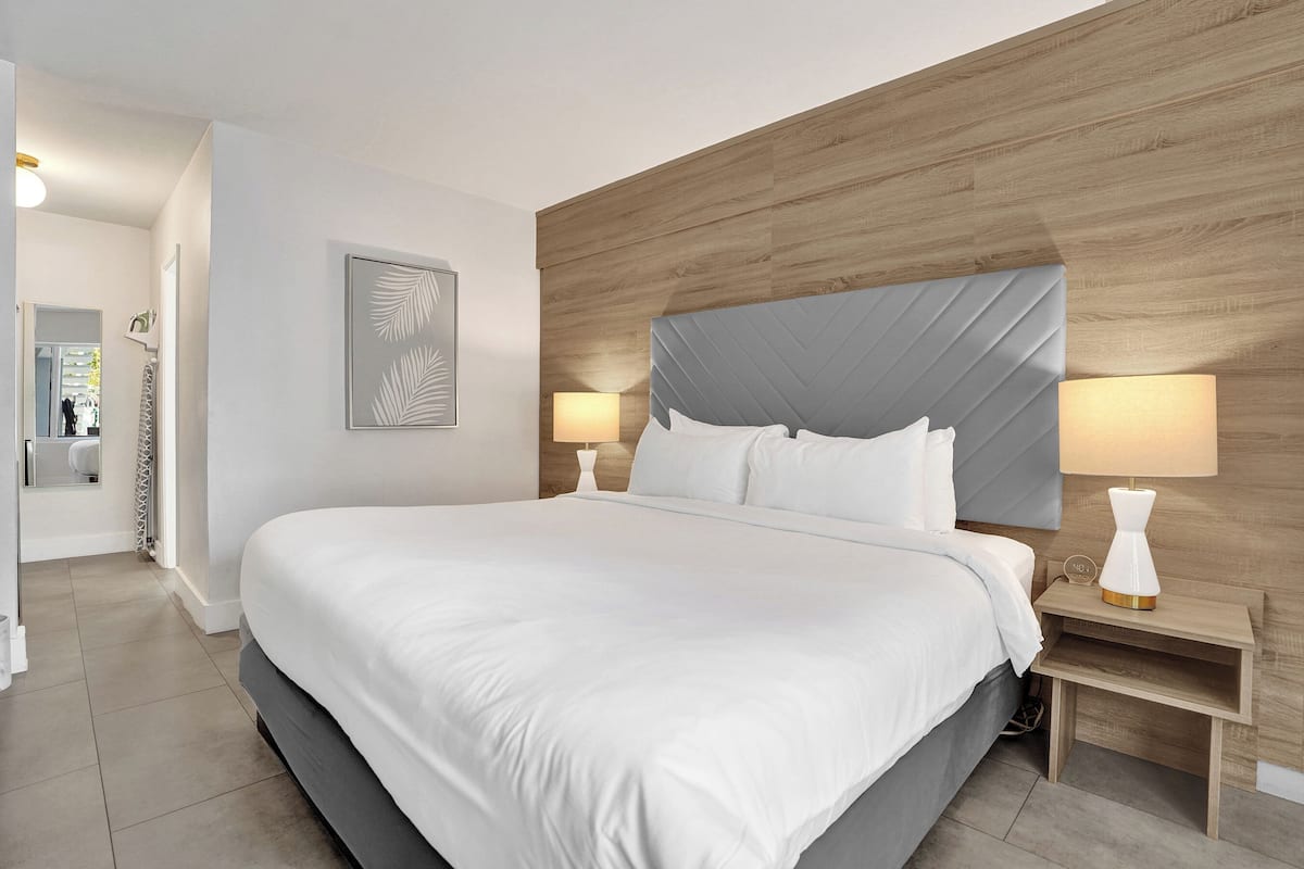 A modern hotel room with a large bed, wooden headboard, two bedside lamps, and a framed artwork on the wall.