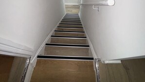 Een smalle trap met houten treden en witte muren, die leidt naar een deur boven.