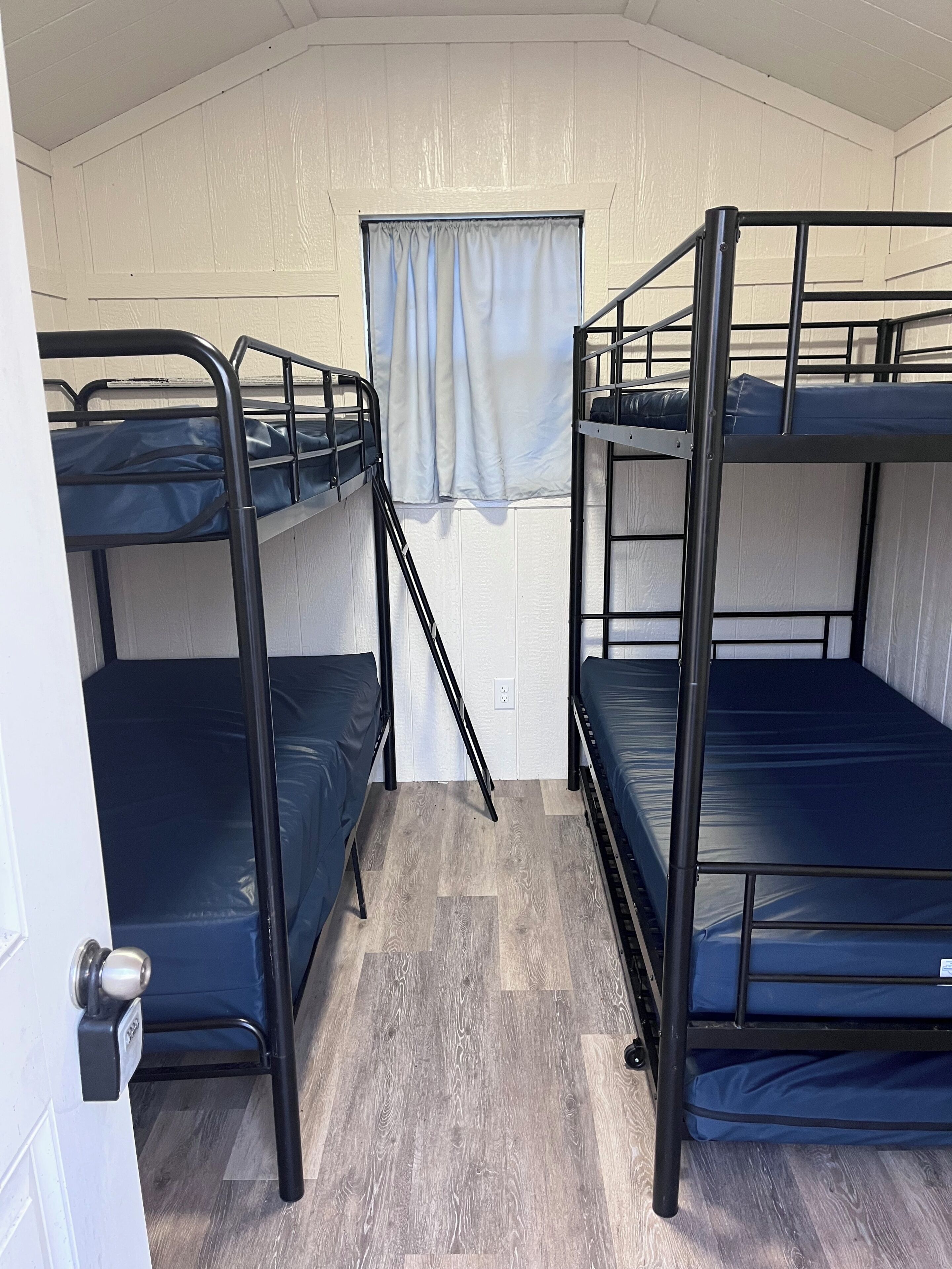 A room with bunk beds, a window with curtains, and a door with a lock.