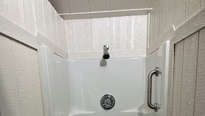 Une cabine de douche blanche, fermée, dotée d’un drain, d’un robinet et d’une barre d’appui.