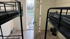 Une chambre avec deux lits superposés, une porte donnant sur l’extérieur et un ventilateur posé sur le sol.