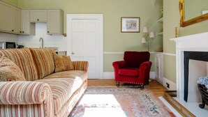 Ein Wohnzimmer mit einem gestreiften Sofa, einem roten Sessel, einem Kamin und einer Küche im Hintergrund.