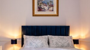 Ein Schlafzimmer mit dunkelblauer Kopfteil, einem gerahmten Gemälde über dem Bett und zwei Nachttischlampen.