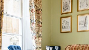 Ein Zimmer mit blauem Sessel, einer gestreiften Couch, einem Tisch mit Gläsern und gerahmten Bildern an der Wand.