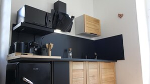 A compact kitchen with a black refrigerator, a microwave, a coffee maker, and wooden cabinets. - The Presbytery Suite (PUISSEGUIN)