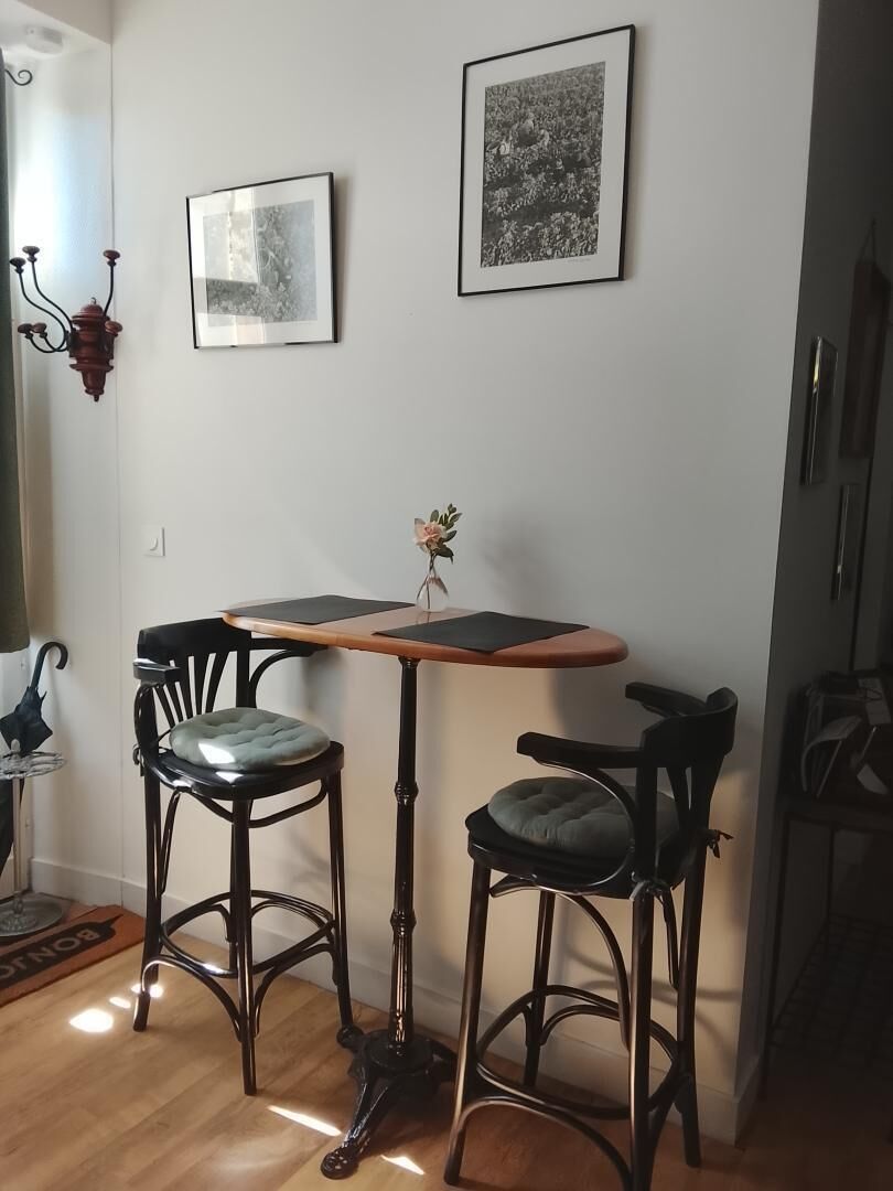Una habitación con dos taburetes, una mesita y dos cuadros en la pared.