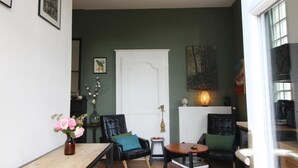 A room with a green wall, a white door, a fireplace, a table with chairs, and a vase with flowers. - The Presbytery Suite (PUISSEGUIN)