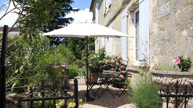 An outdoor patio with a table and chairs, surrounded by potted plants and flowers. - The Presbytery Suite (PUISSEGUIN)