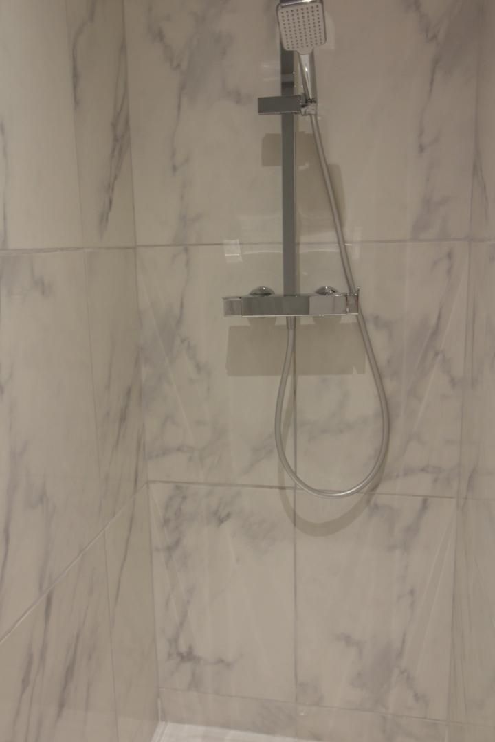 A shower with a handheld showerhead and a handheld hose against a marble wall.