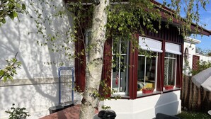 A white building with a red roof, a window with white shutters, a tree in front, and a barbecue grill. - Charme d'Arès - ARES - Gîte (ARES)