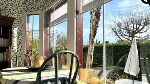 A room with a large window, a table with chairs, a bookshelf, and a potted plant. - Charme d'Arès - ARES - Gîte (ARES)