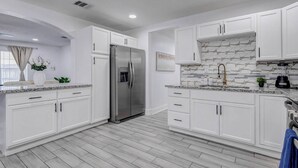 A modern kitchen with white cabinetry, a stainless steel refrigerator, a marble backsplash, and a window with curtains. - Beautiful Luxury Retreat in Downtown Houston minutes to NRG/UT/Med Ctr/Zoo/ UH (Houston)