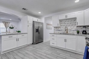 A modern kitchen with white cabinetry, a stainless steel refrigerator, a marble backsplash, and a window with curtains. - Beautiful Luxury Retreat in Downtown Houston minutes to NRG/UT/Med Ctr/Zoo/ UH (Houston)