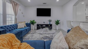 A living room with a blue sofa, a glass coffee table, and a flat-screen TV mounted on the wall. - Beautiful Luxury Retreat in Downtown Houston minutes to NRG/UT/Med Ctr/Zoo/ UH (Houston)