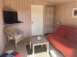 A room with a television on a shelf, a wicker chair, a red sofa, a small table with a decorative ball, and a door with curtains. - Les Oyats - ANDERNOS-LES-BAINS (ANDERNOS-LES-BAINS)