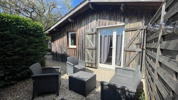 Eine Holzhütte mit Terrasse, auf der Korbmöbel stehen, und einem Kiesweg.