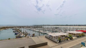Un port de plaisance avec des bateaux amarrés, une plage en arrière-plan et un café doté d’une terrasse.