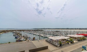 A marina with boats docked, a beach in the background, and a café with outdoor seating. - Sea-view studio by the port | 2 guests | Ref 2000 (ST CAST LE GUILDO)