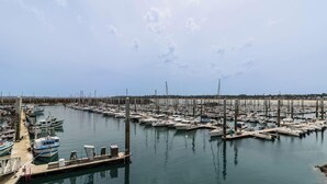 Un port de plaisance où sont amarrés de nombreux bateaux, une plage de sable en arrière-plan et un ciel dégagé.