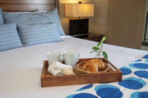 Ein ordentlich bezogenes Bett mit einem Tablett Croissants, zwei weißen Tassen und einem zusammengerollten Handtuch.