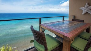 Una mesa de madera con cojines verdes, una silla de mimbre y una decoración con estrella de mar en un balcón con vistas al océano.