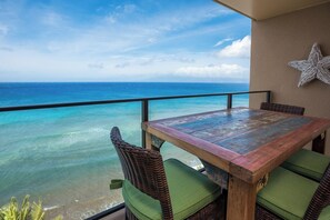 Ein Holztisch mit grünen Kissen, ein Korbstuhl und eine Meerstern-Dekoration auf einem Balkon mit Blick auf das Meer.